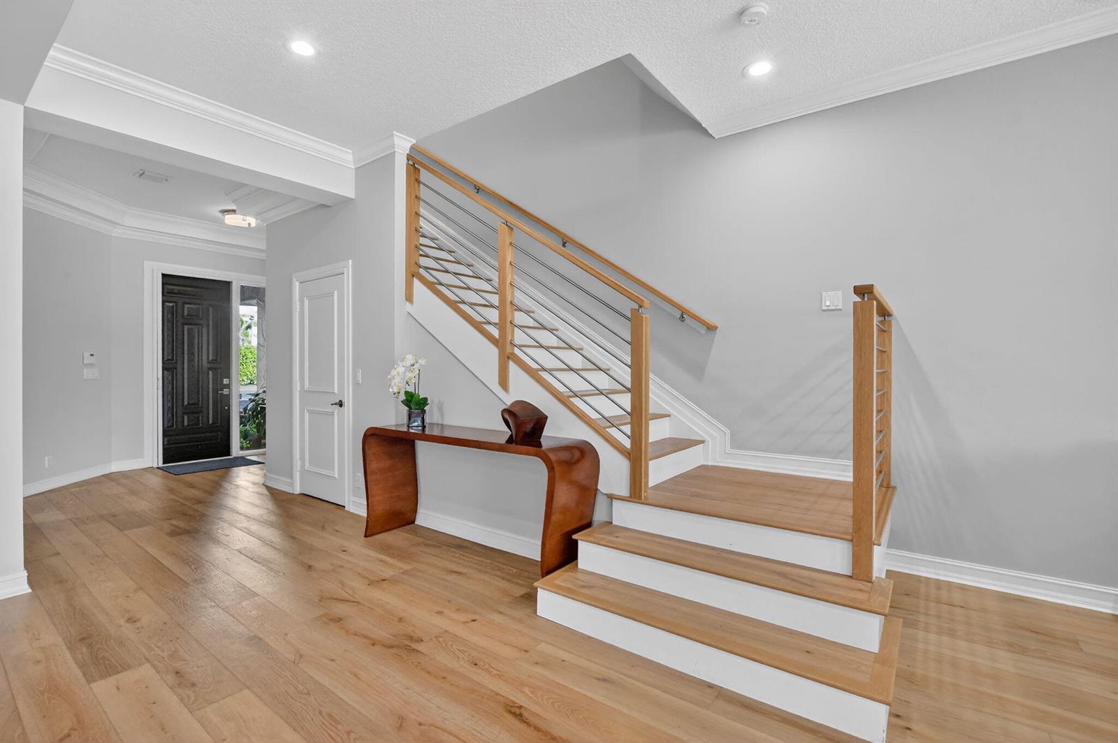 A foyer features light wood flooring, a wooden console table, and a staircase with railings — 1535 Estuary Trail, Delray Beach FL 33483, DELRAY BEACH, FL