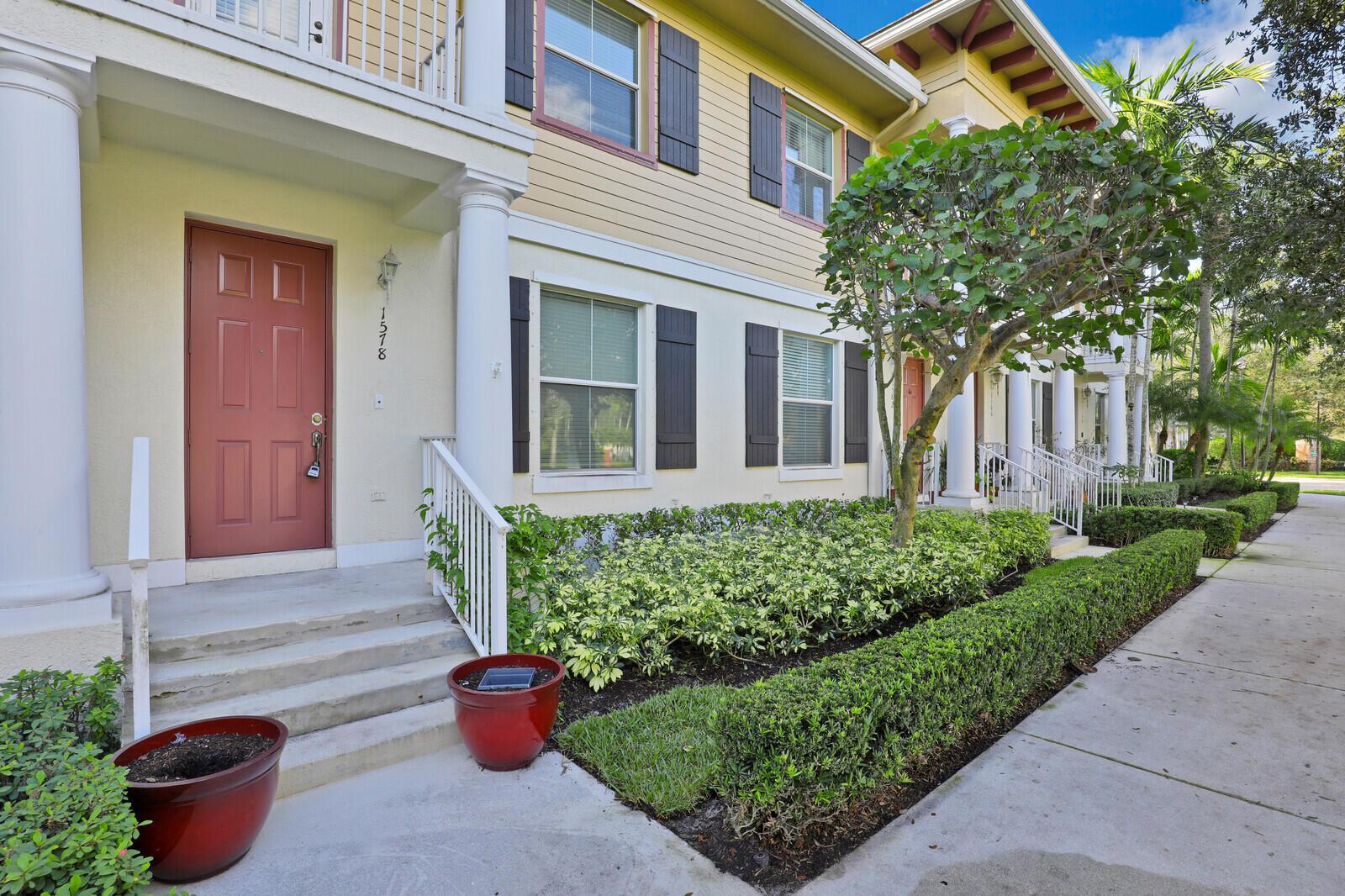 A two-story townhouse exterior features a red front door, white columns, and manicured landscaping — 1578 Frederick Small Road, Jupiter FL 33458, JUPITER, FL