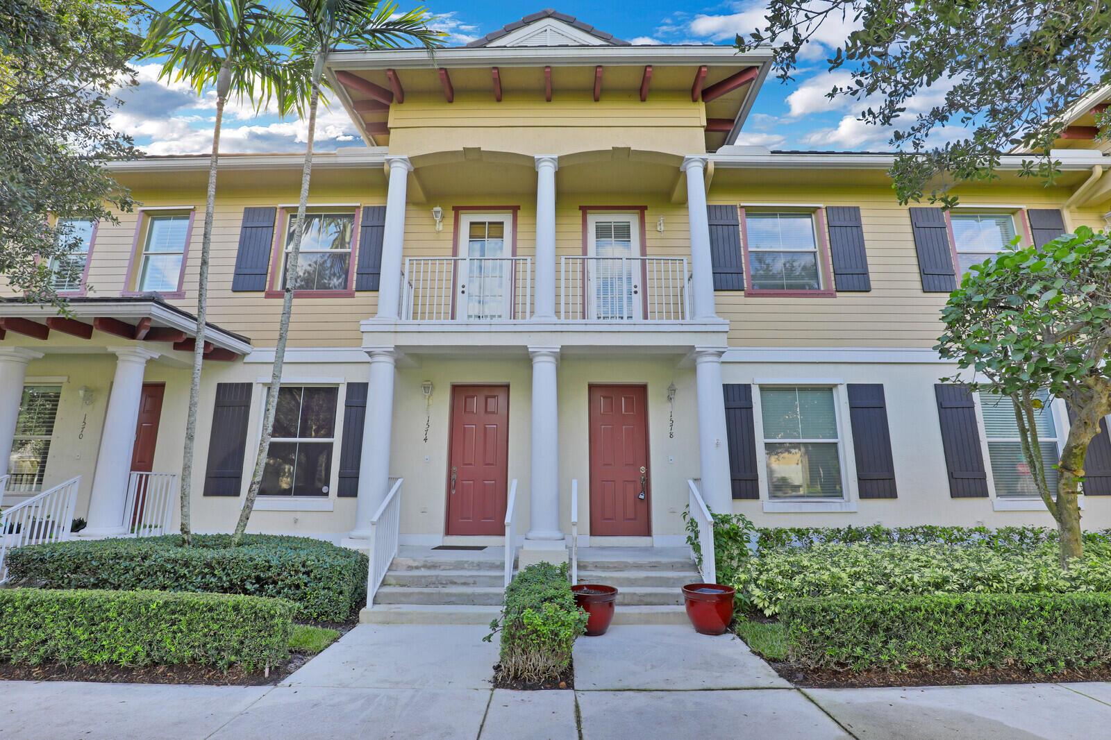 A two-story townhouse exterior features yellow siding, white columns, and two red front doors — 1578 Frederick Small Road, Jupiter FL 33458, JUPITER, FL