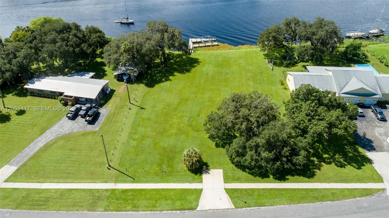 An aerial view shows a vacant grassy lot situated between two houses near a lake — 395 Old County Road 78, La Belle FL 33935, LA BELLE, FL