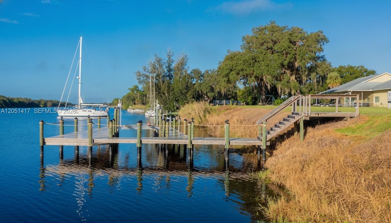A wooden dock extends into a calm waterway near a grassy bank and trees — 395 Old County Road 78, La Belle FL 33935, LA BELLE, FL