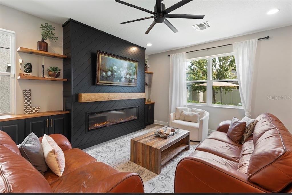 A living room features a black diagonal-plank fireplace wall, leather sofas, and a wood coffee table — 19364 BREYNIA DRIVE, LUTZ, FL