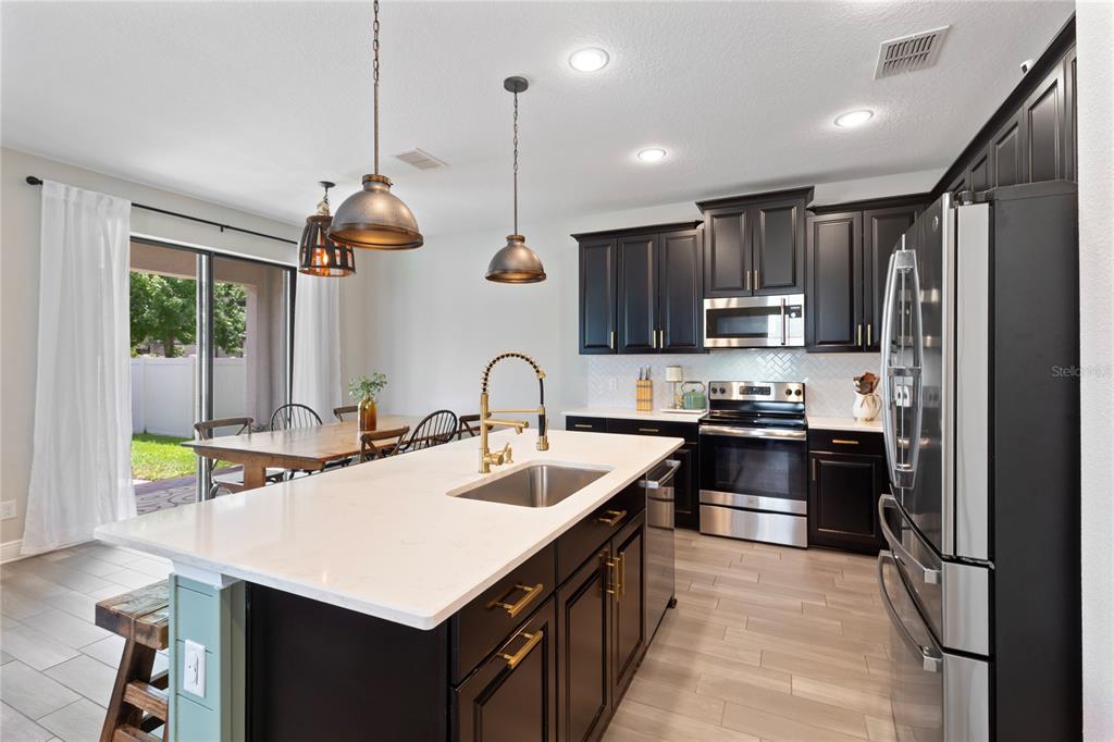 A kitchen features dark cabinets, a white quartz island with a sink, and stainless appliances — 19364 BREYNIA DRIVE, LUTZ, FL