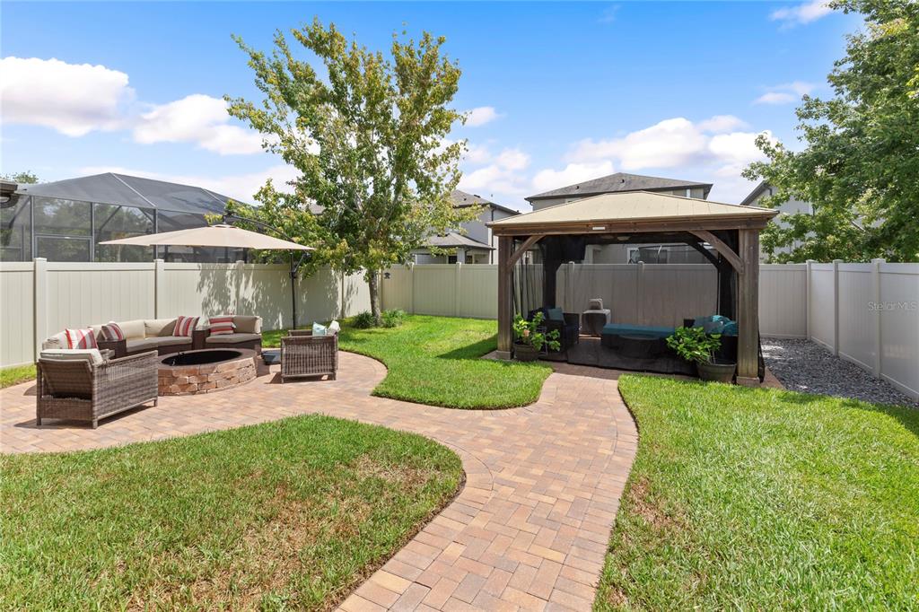 A backyard features a paver patio with a fire pit, seating, and a wooden gazebo — 19364 BREYNIA DRIVE, LUTZ, FL