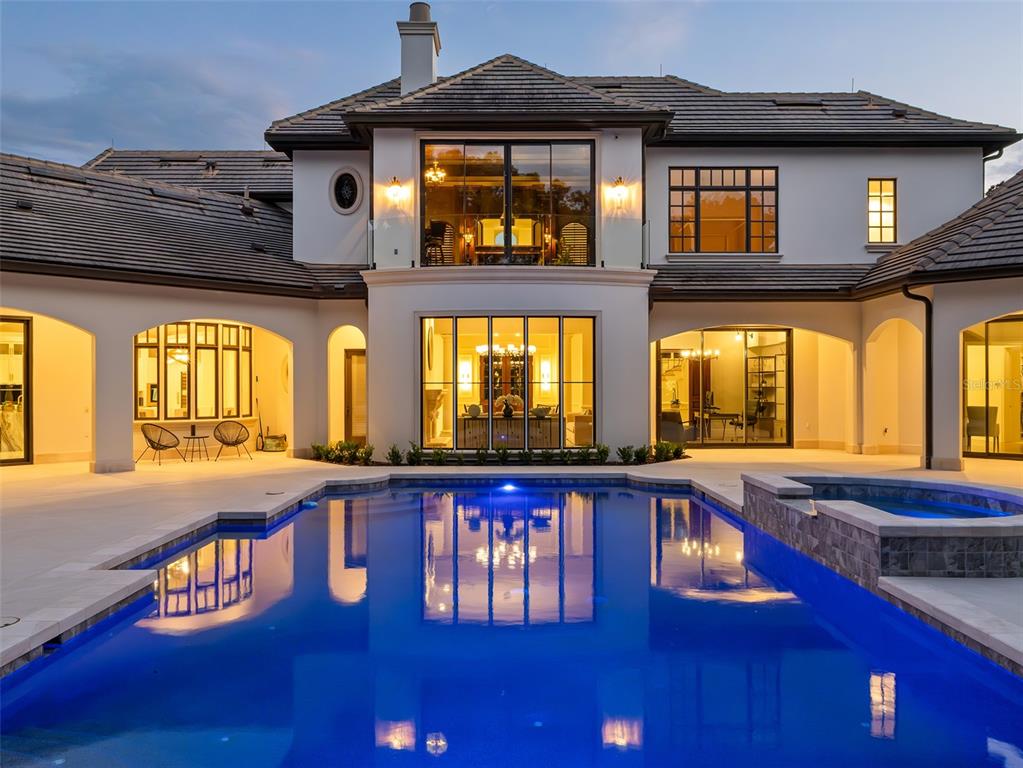 A two-story house exterior with a swimming pool, patio, and large glass windows at dusk — 9921 LAKE LOUISE DRIVE, WINDERMERE, FL