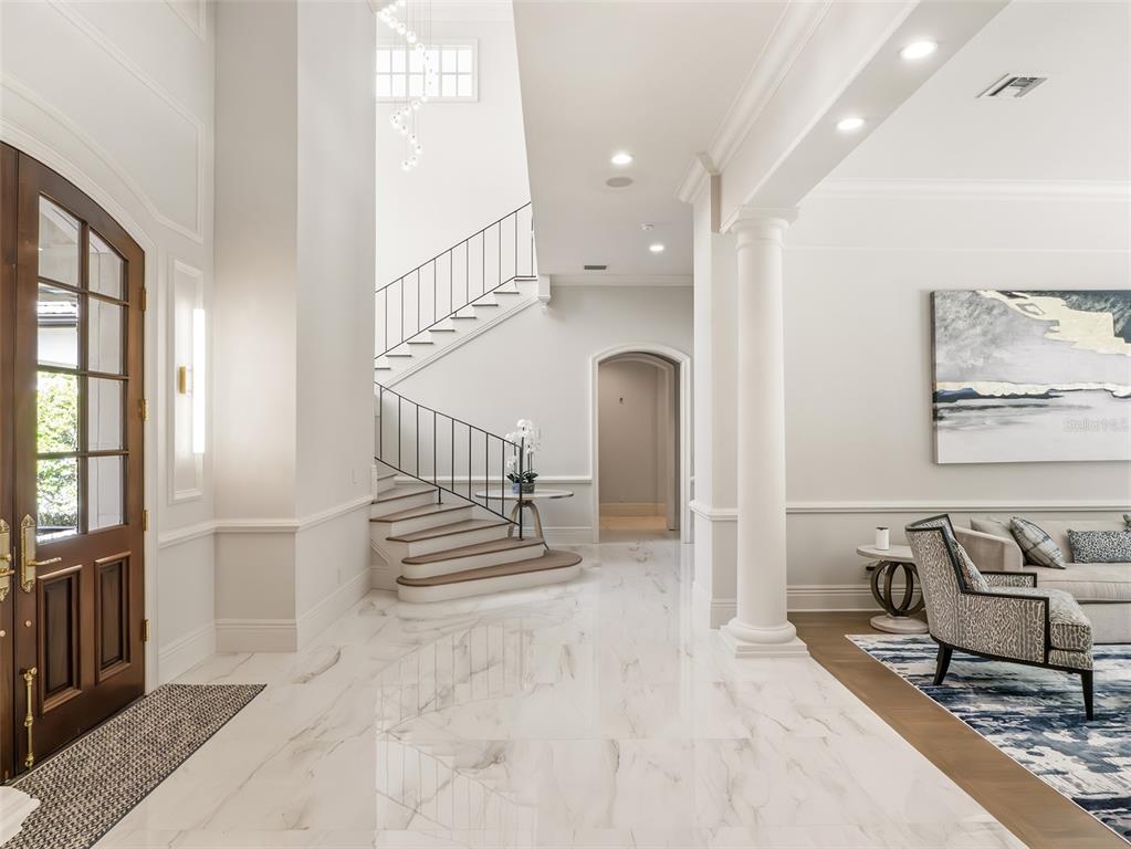 A bright foyer features marble flooring, a curved staircase with iron railings, and a white column — 9921 LAKE LOUISE DRIVE, WINDERMERE, FL