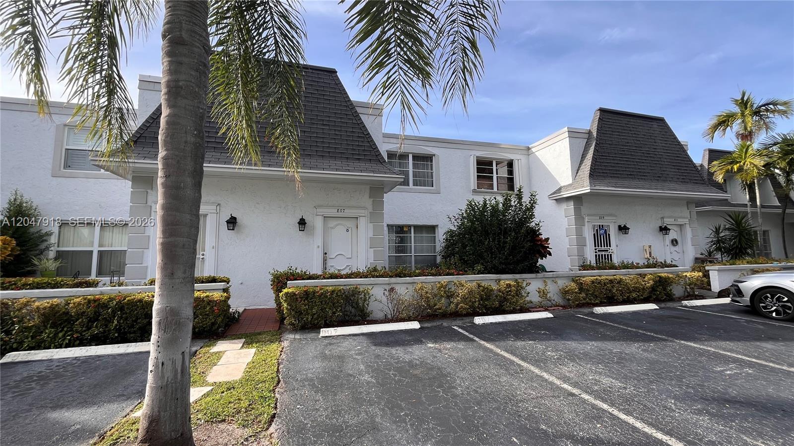 The exterior of a two-story white townhouse complex features dark shingled mansard roofs and parking — 807 NE 27th Ave # 807, Hallandale Beach FL 33009, HALLANDALE BEACH, FL
