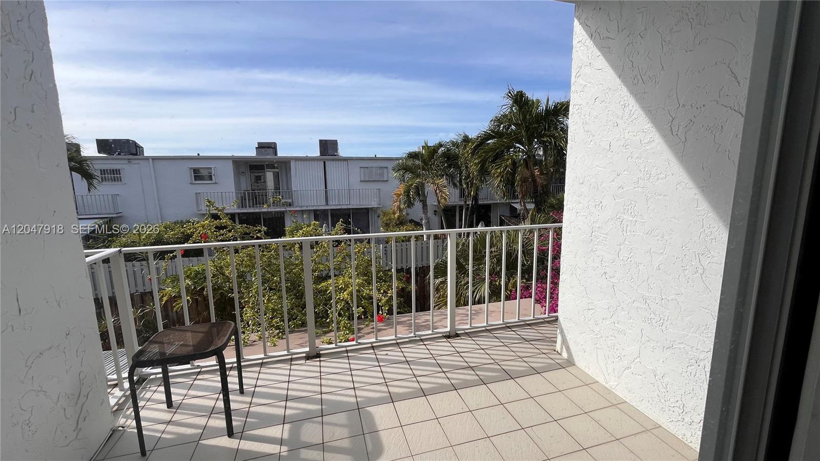 A balcony with tiled flooring, a metal railing, and a small chair overlooks palm trees — 807 NE 27th Ave # 807, Hallandale Beach FL 33009, HALLANDALE BEACH, FL