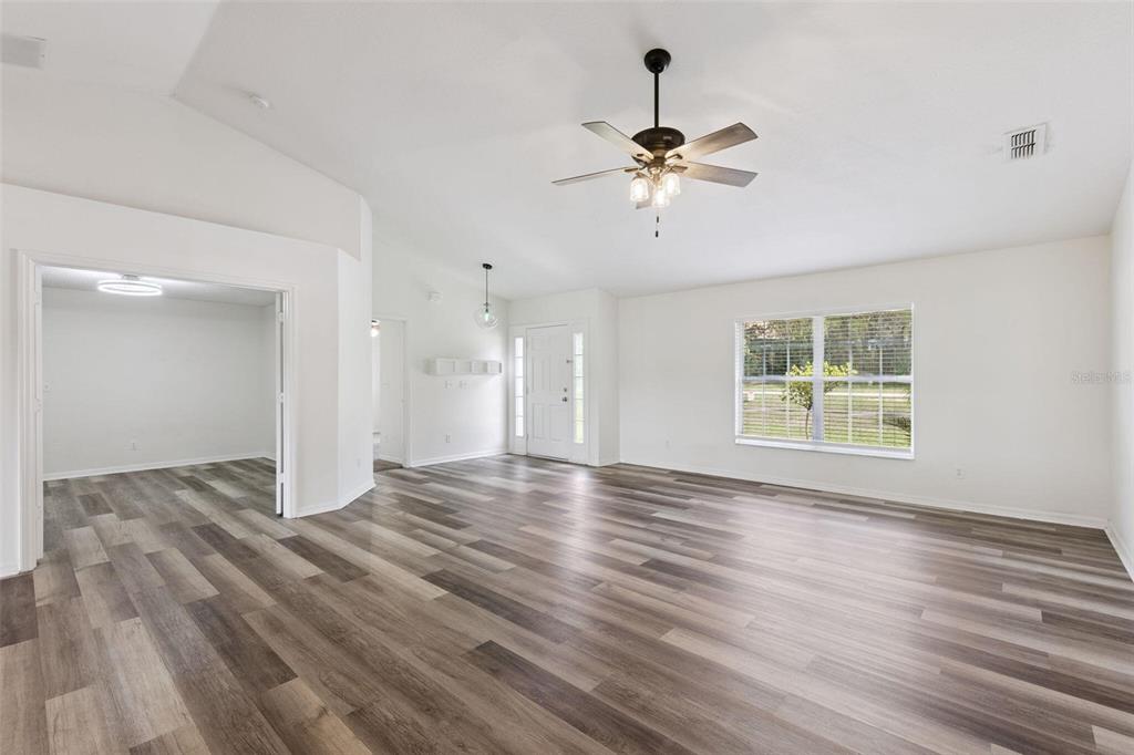 A spacious living room features light-colored walls, wood-look vinyl flooring, and a ceiling fan — 1348 GOLDEN POND DRIVE, MINNEOLA, FL