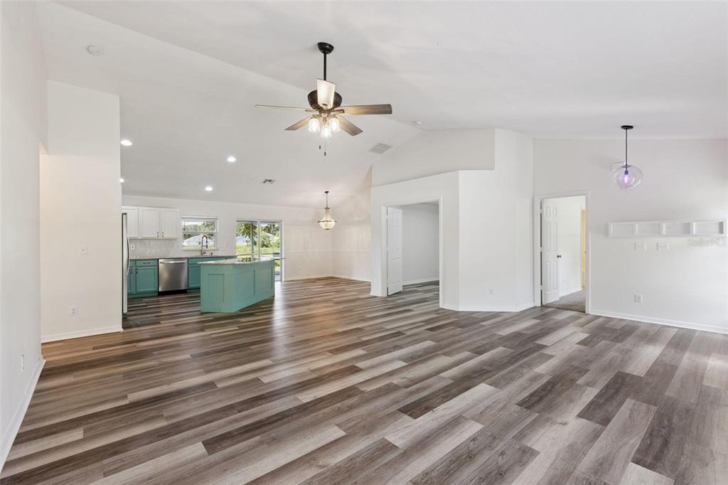 An open-concept living area features wood-look flooring, a kitchen with teal cabinetry, and vaulted ceilings — 1348 GOLDEN POND DRIVE, MINNEOLA, FL