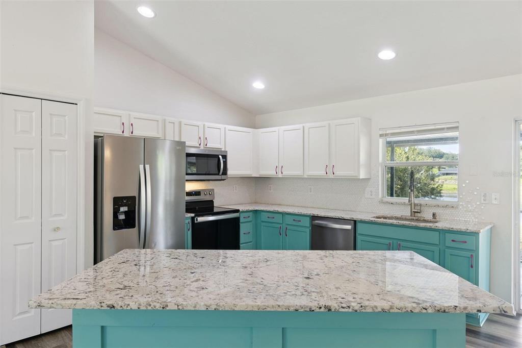A kitchen features white upper cabinets, teal lower cabinets, granite countertops, and stainless steel appliances — 1348 GOLDEN POND DRIVE, MINNEOLA, FL