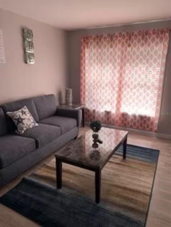 A living room features a gray sofa, a marble-topped coffee table, and patterned pink curtains — 3100 PARKWAY BOULEVARD UNIT 422, KISSIMMEE, FL