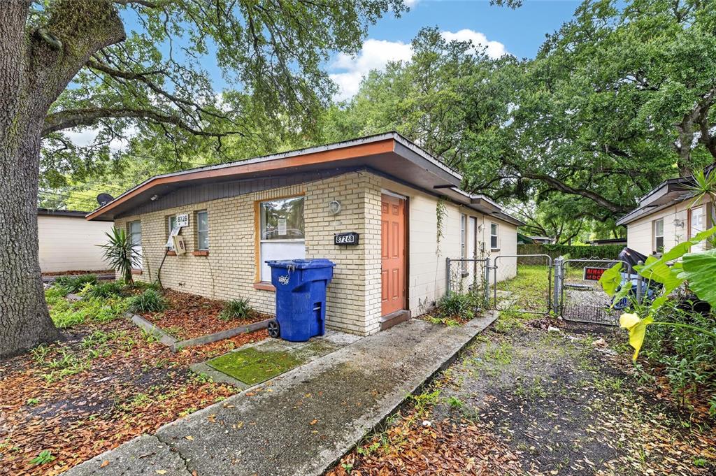 A single-story brick duplex building features a concrete walkway, a blue trash bin, and trees — 8726 & 8728 N 48TH STREET, TAMPA, FL