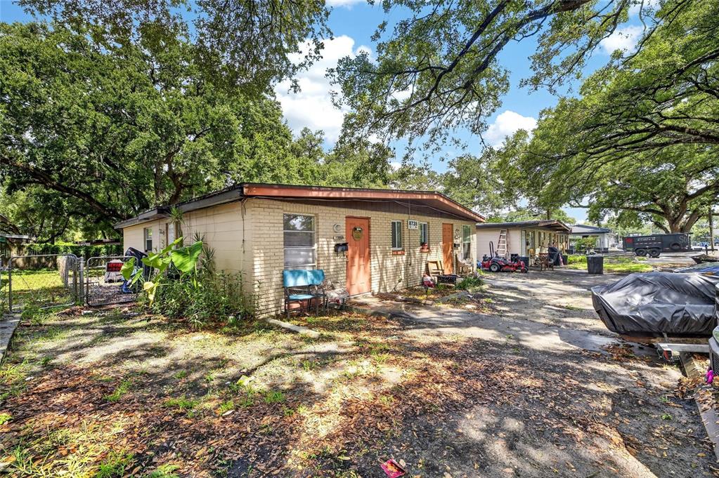 A single-story brick duplex with two orange doors sits on a dirt lot under trees — 8726 & 8728 N 48TH STREET, TAMPA, FL