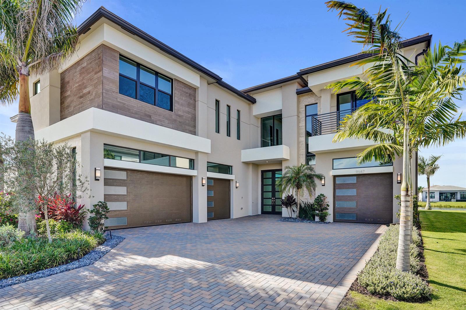 A modern two-story house features a paved driveway, three garage doors, and palm trees — 9547 Riverside Park Drive, Boca Raton FL 33434, BOCA RATON, FL