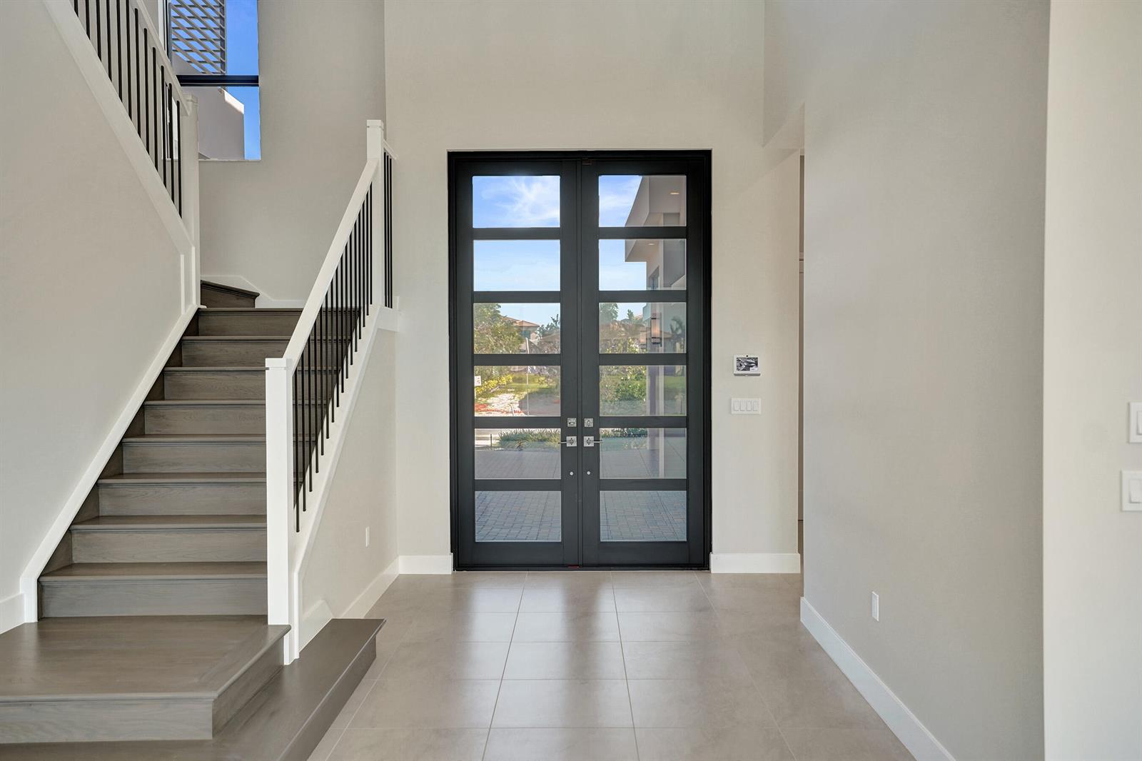 A bright entryway features a double glass door, tiled floors, and a wooden staircase — 9547 Riverside Park Drive, Boca Raton FL 33434, BOCA RATON, FL