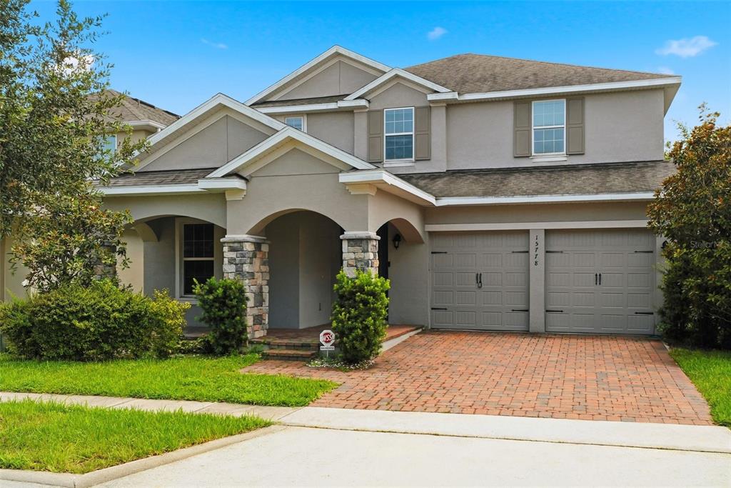 A two-story suburban house with a stone-accented porch, gray garage doors, and brick driveway — 15778 SWEET LIMETTA DRIVE, WINTER GARDEN, FL