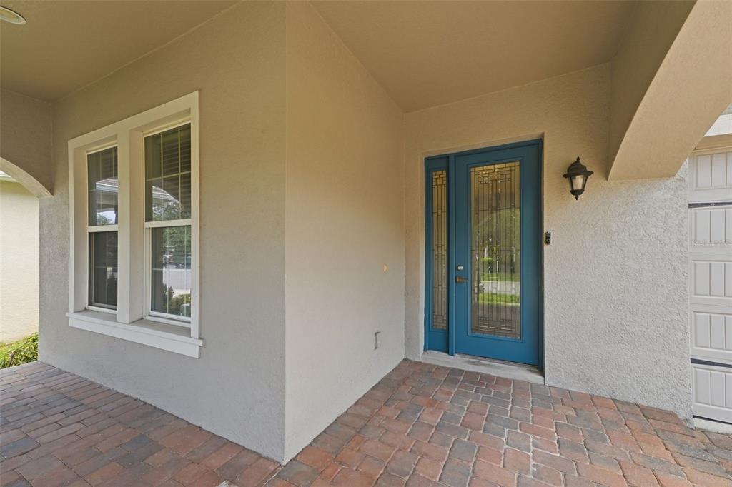 A covered entryway features a blue front door with glass panels and brick paver flooring — 15778 SWEET LIMETTA DRIVE, WINTER GARDEN, FL