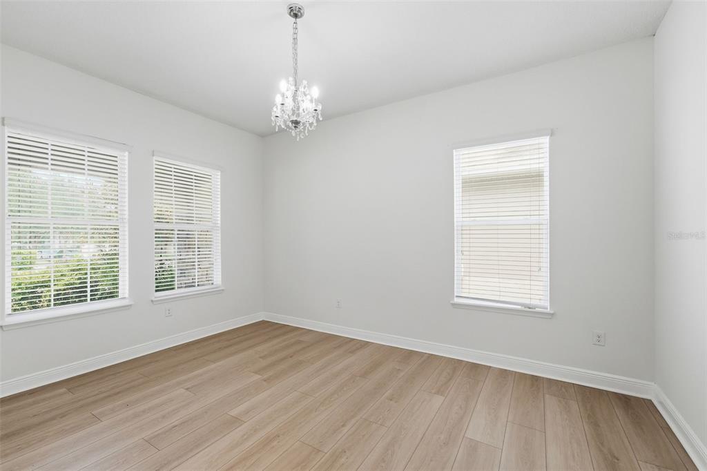 An empty room features light wood-look flooring, white walls, three windows with blinds, and a chandelier — 15778 SWEET LIMETTA DRIVE, WINTER GARDEN, FL