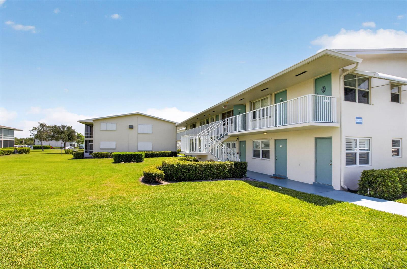 A two-story apartment building with white stucco walls, teal doors, and a metal staircase — 660 Horizon W # 107, Boynton Beach FL 33435, BOYNTON BEACH, FL