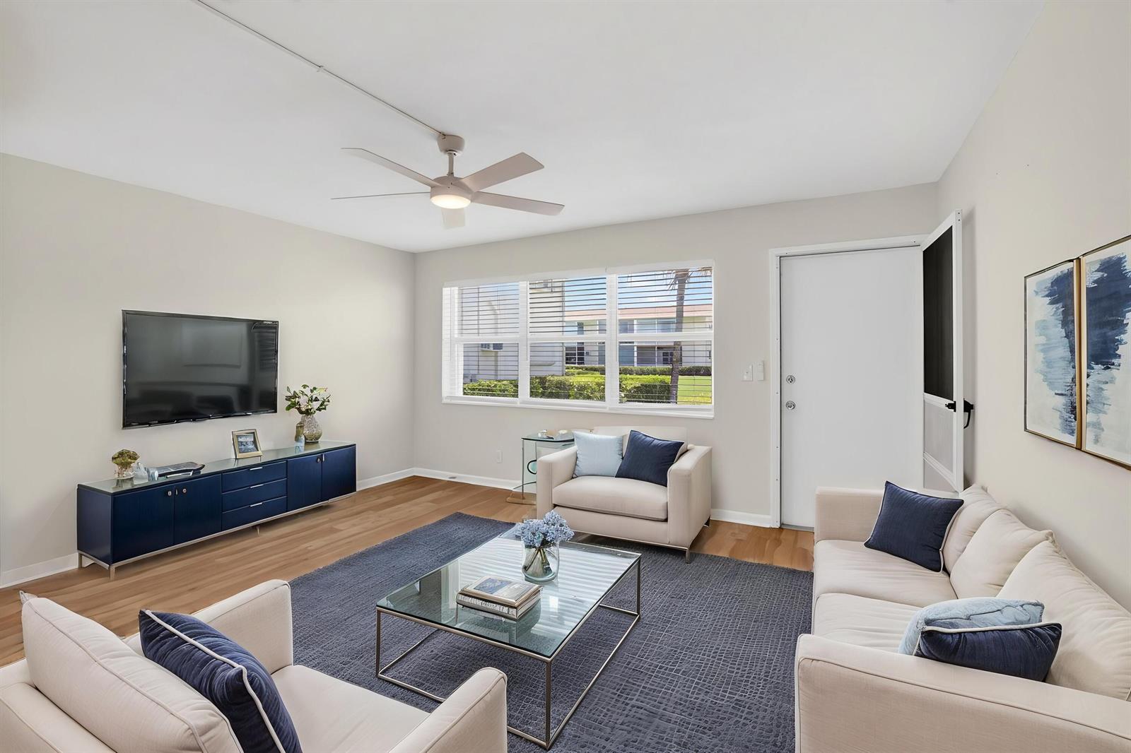 A living room features a blue media console, a glass coffee table, and light-colored furniture — 660 Horizon W # 107, Boynton Beach FL 33435, BOYNTON BEACH, FL