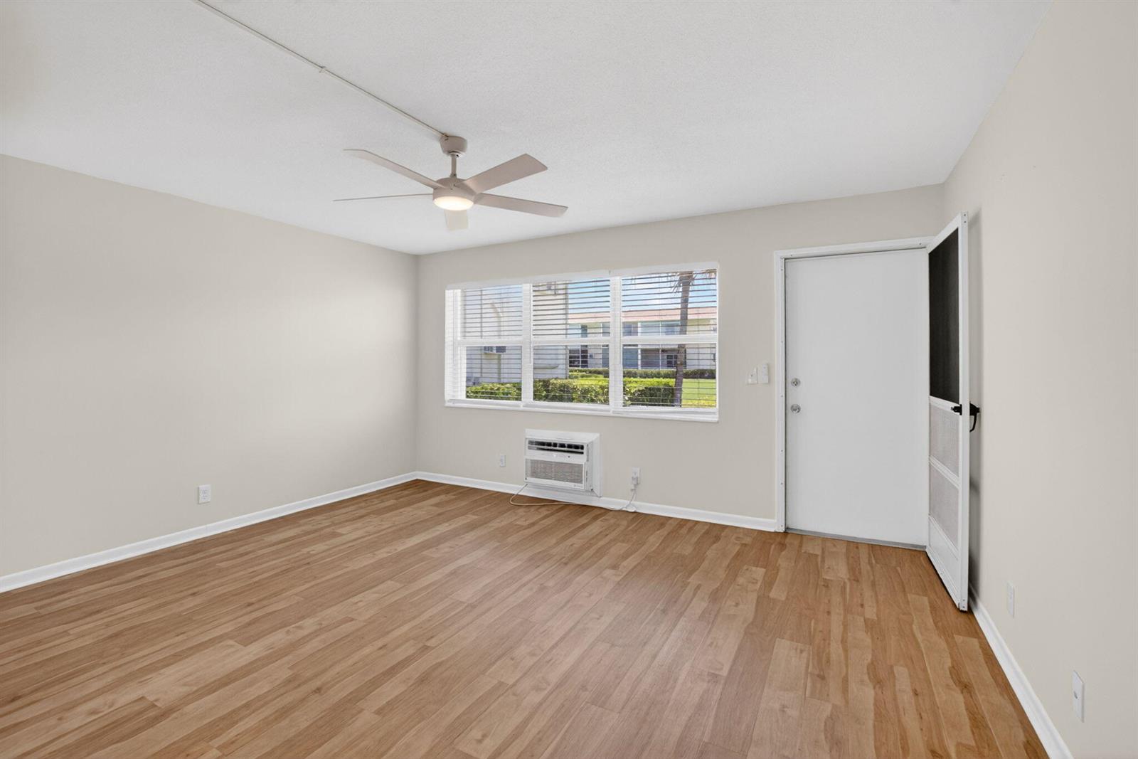 An empty room features light wood-look flooring, a ceiling fan, and a window air conditioner — 660 Horizon W # 107, Boynton Beach FL 33435, BOYNTON BEACH, FL