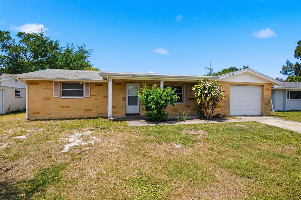A single-story house with a tan brick exterior, a front porch, and an attached garage — 8739 LIDO LANE, PORT RICHEY, FL