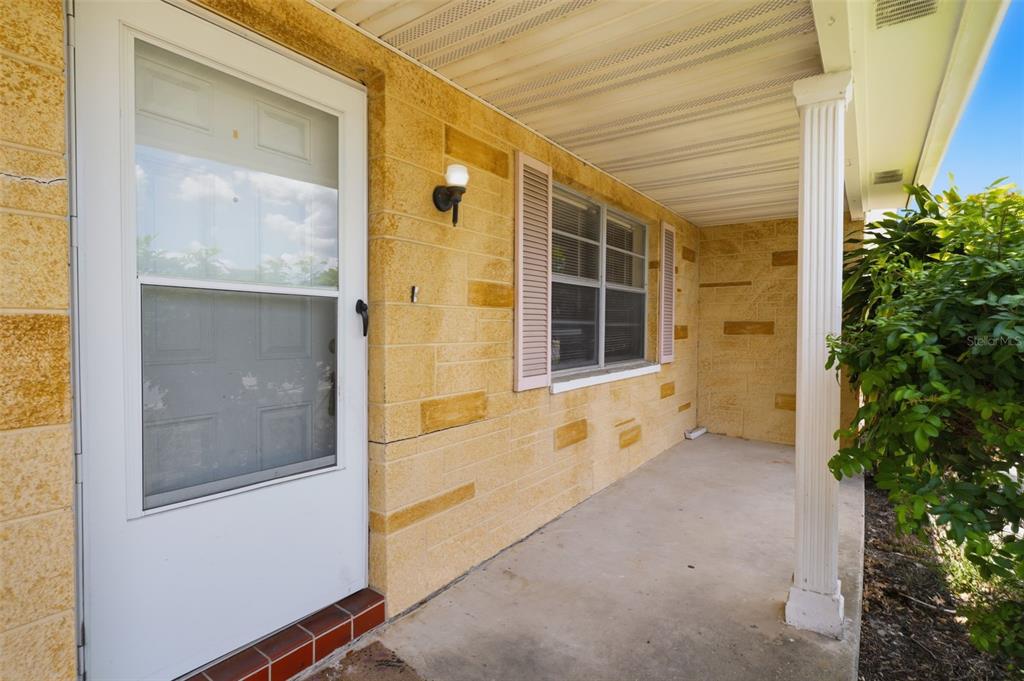 A covered concrete porch features yellow stone walls, a white storm door, and a column — 8739 LIDO LANE, PORT RICHEY, FL