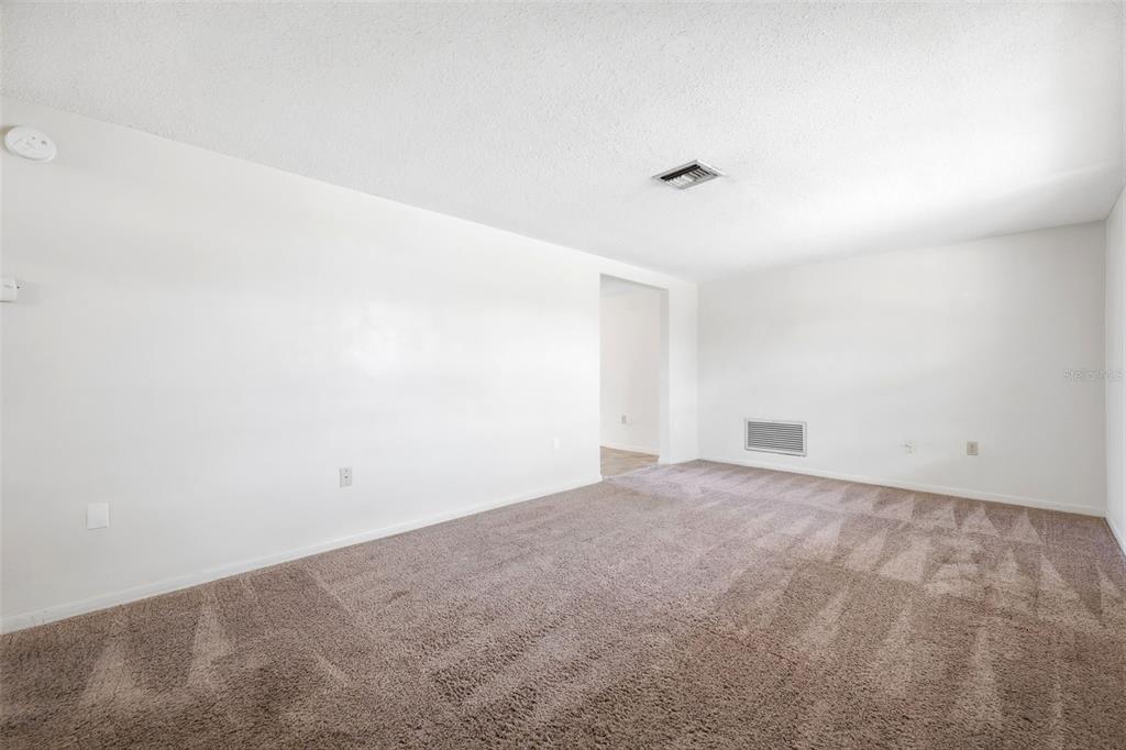 An empty room with white walls, beige carpet, and a doorway leading to another area — 8739 LIDO LANE, PORT RICHEY, FL