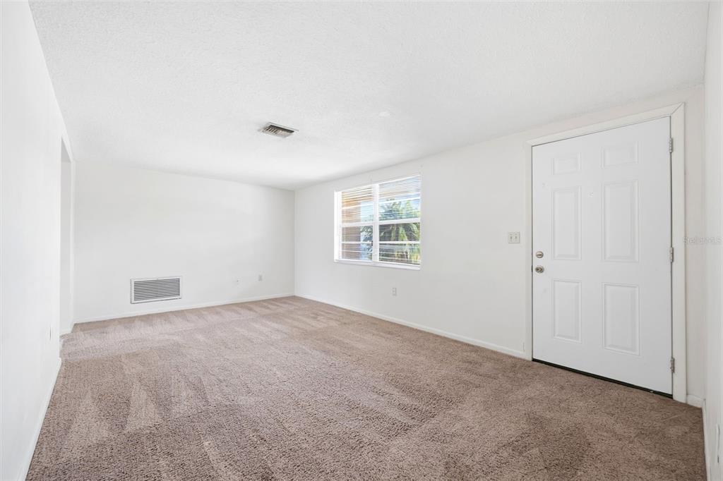 An empty room with beige carpet, white walls, a window with blinds, and a white door — 8739 LIDO LANE, PORT RICHEY, FL