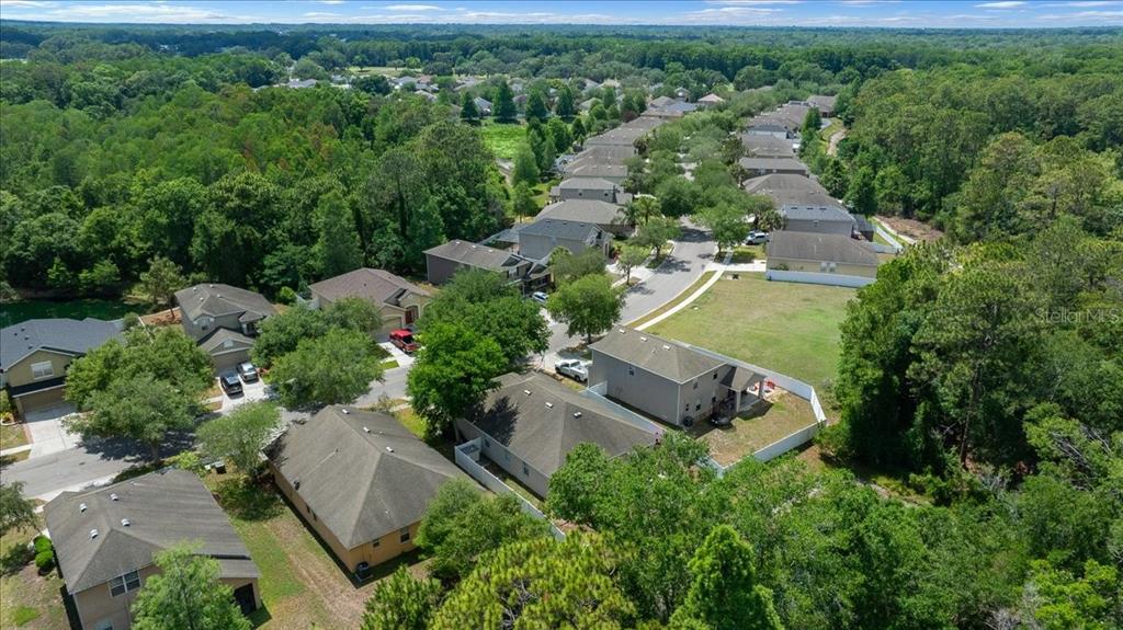 An aerial view shows a suburban neighborhood with houses, green lawns, and surrounding forest — 12044 COLONY LAKES BOULEVARD, NEW PORT RICHEY, FL