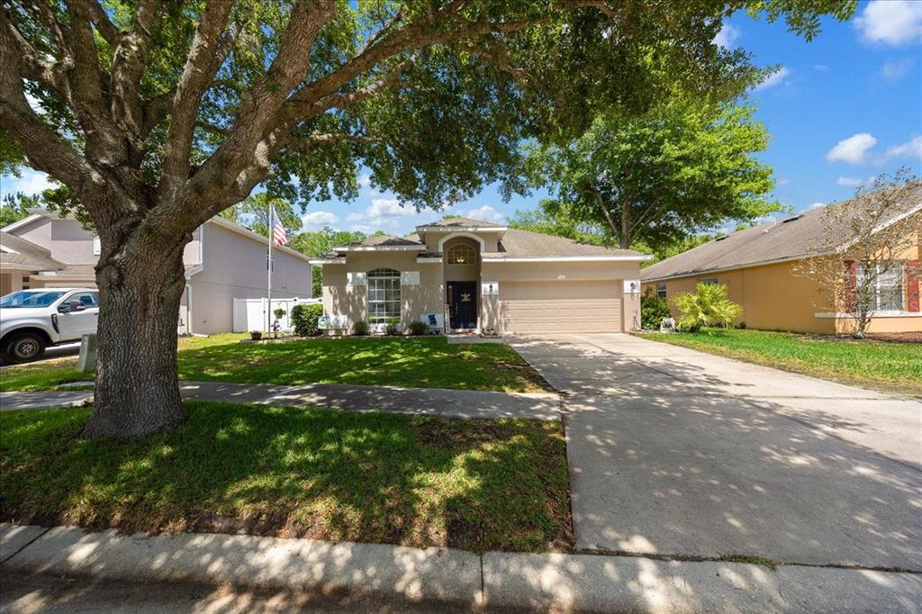 A single-story suburban house with a tan exterior, a two-car garage, and a large tree — 12044 COLONY LAKES BOULEVARD, NEW PORT RICHEY, FL