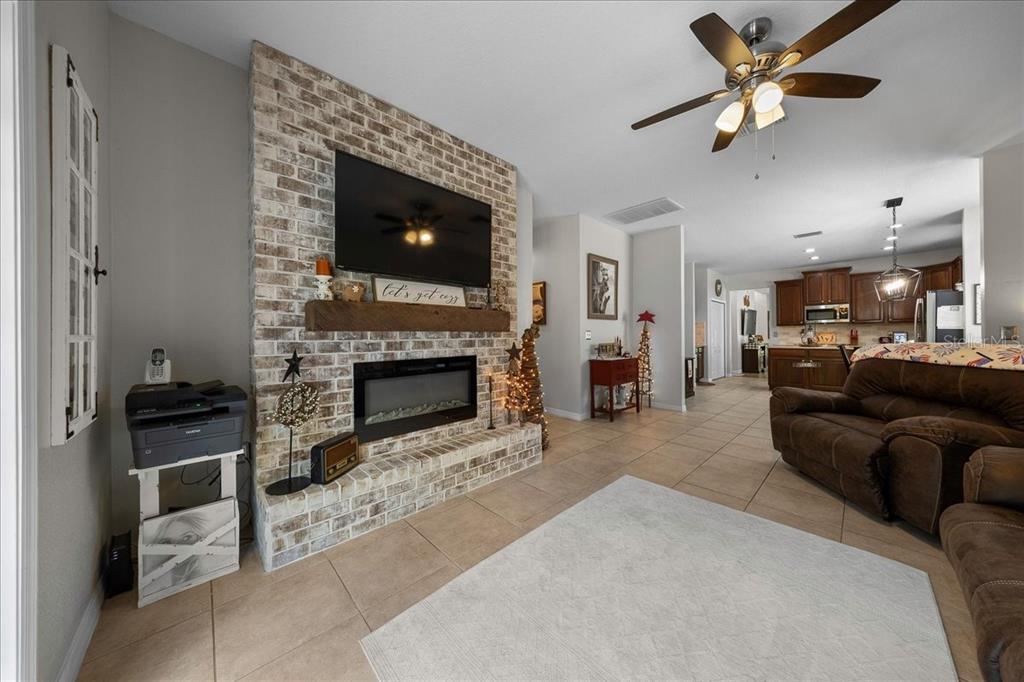 A living room features a brick fireplace with a mounted television and an open kitchen — 12044 COLONY LAKES BOULEVARD, NEW PORT RICHEY, FL