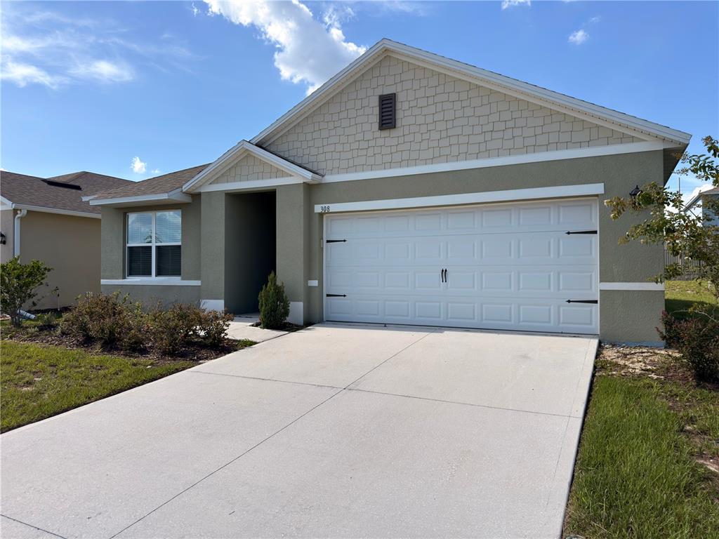 A single-story house features a two-car garage, light-colored stucco walls, and a shingled gable roof — 308 SOFIA LANE, LAKE ALFRED, FL