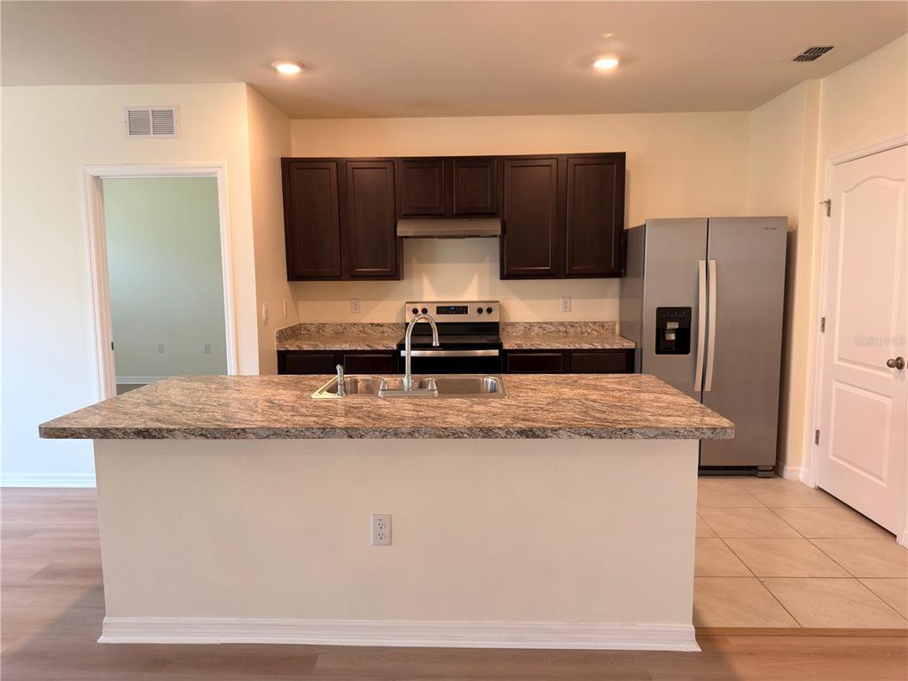 A kitchen features a granite-topped island, dark wood cabinets, and stainless steel appliances — 308 SOFIA LANE, LAKE ALFRED, FL