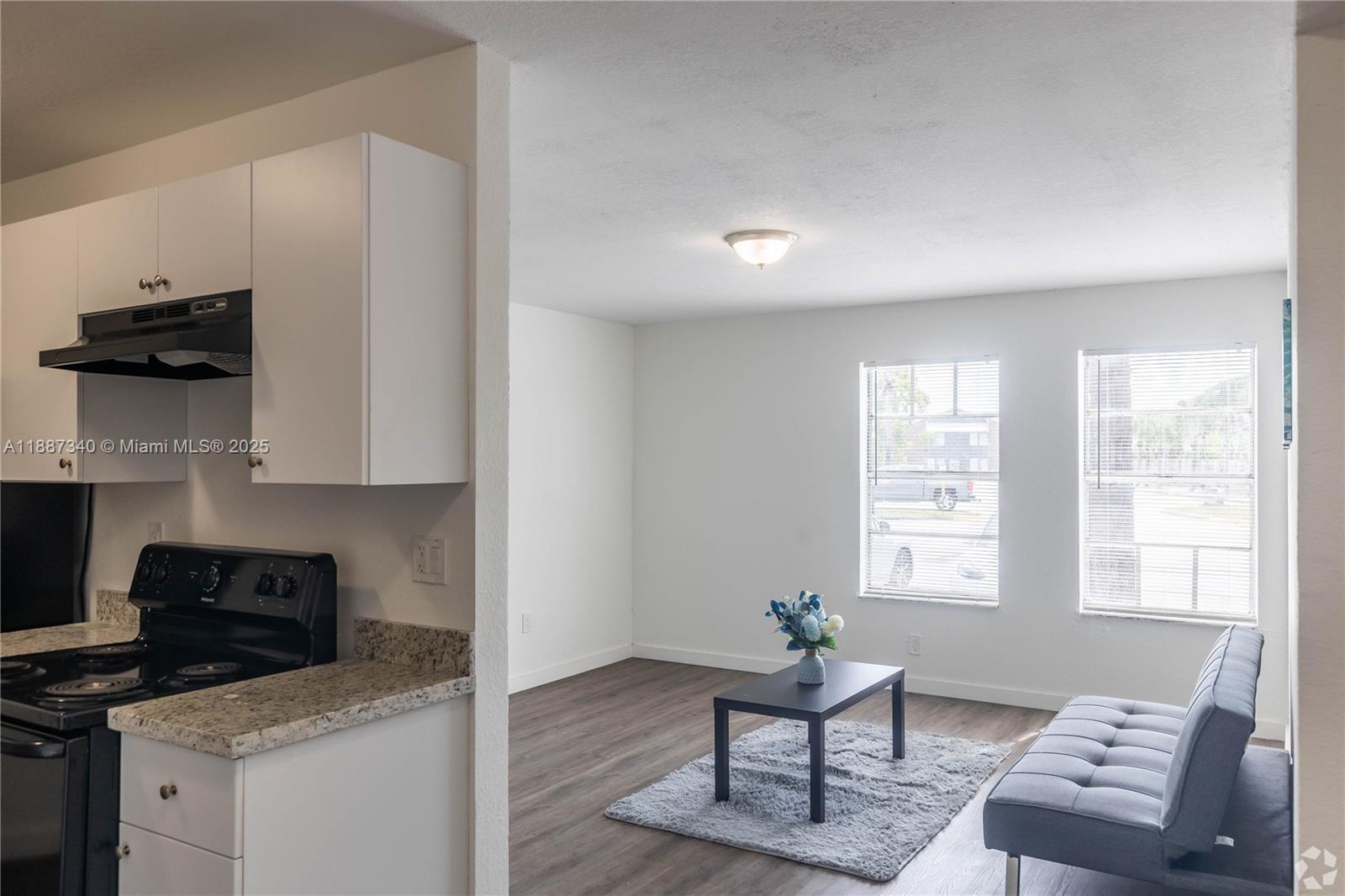 A kitchen with white cabinets and granite countertops opens into a living area with windows — 2000 S Main Street # 000, Belle Glade FL 33430, BELLE GLADE, FL