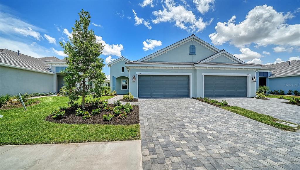 A light blue duplex house features two gray garage doors and a paved driveway — 2324 BLUE MAHOE LANE, SARASOTA, FL