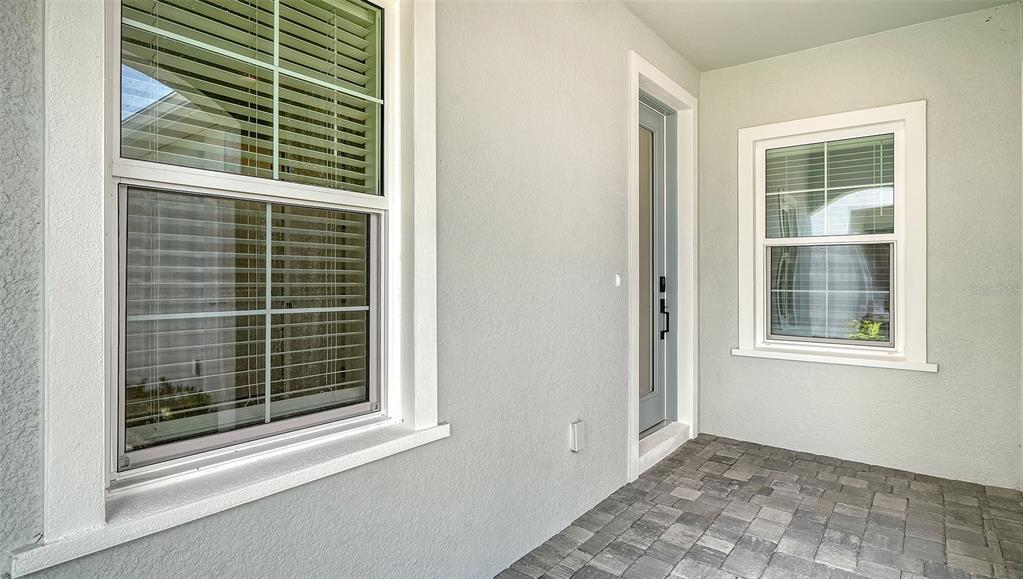 A covered entryway features light-colored stucco walls, two windows with blinds, and stone pavers — 2324 BLUE MAHOE LANE, SARASOTA, FL