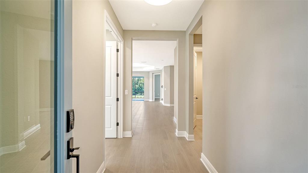 A view from an entryway looking down a hallway toward a living area with windows — 2324 BLUE MAHOE LANE, SARASOTA, FL