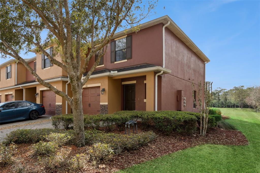 A two-story townhouse with a brown stucco exterior, a garage, and a landscaped front yard — 601 JOYFUL BLOSSOM PLACE, LONGWOOD, FL