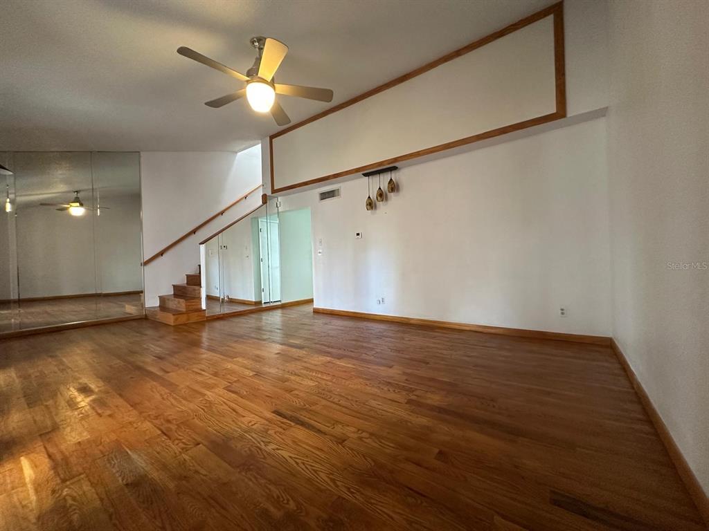 An empty living room features hardwood floors, a ceiling fan, and a staircase with mirrors — 5419 SWEETWATER TERRACE CIRCLE UNIT 3-20, TAMPA, FL
