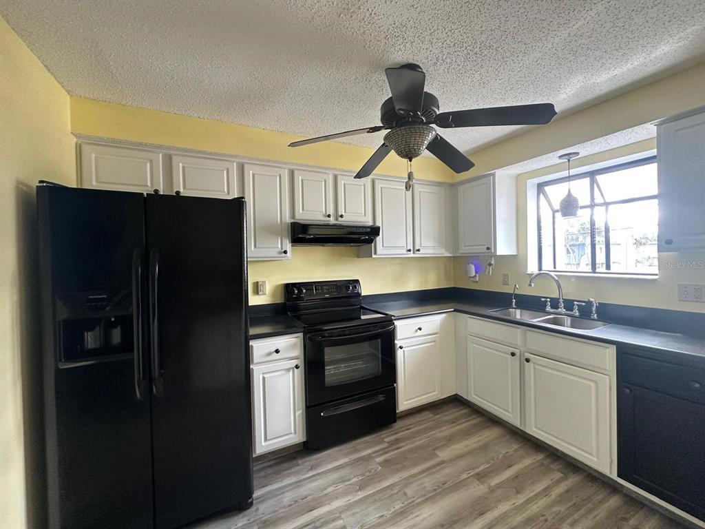A kitchen features white cabinets, black appliances, a ceiling fan, and wood-look flooring — 5419 SWEETWATER TERRACE CIRCLE UNIT 3-20, TAMPA, FL