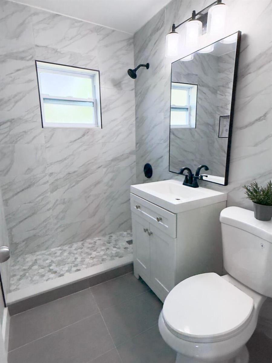 A bathroom features a marble-tiled shower, a white vanity, a mirror, and a toilet — 2533 NE 12th Terrace, Pompano Beach FL 33064, POMPANO BEACH, FL