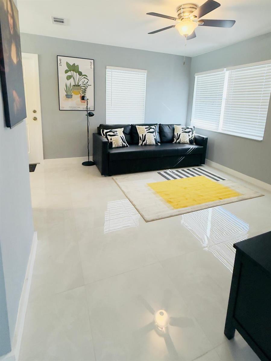 A living room features a black sofa, a yellow and white rug, and tile flooring — 2533 NE 12th Terrace, Pompano Beach FL 33064, POMPANO BEACH, FL