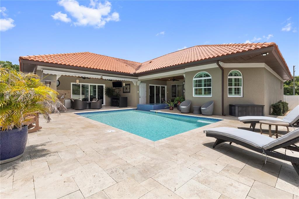 A backyard features a swimming pool, stone patio, lounge chairs, and a covered outdoor living area — 2101 W BEARSS AVENUE, TAMPA, FL