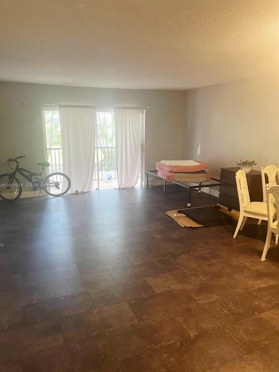 A room with dark tile flooring, a bicycle, a bed frame, and dining chairs — LAUDERHILL, FL