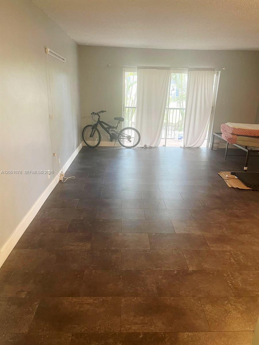 This room features dark tile flooring, a sliding glass door with curtains, and a bicycle — LAUDERHILL, FL