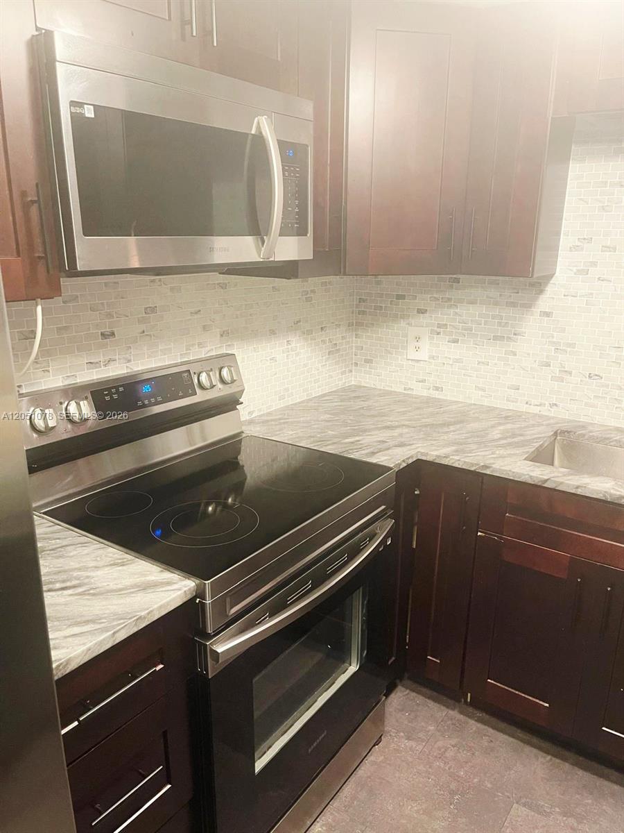 A kitchen features dark wood cabinets, a stainless steel stove, and a marble-patterned countertop — LAUDERHILL, FL