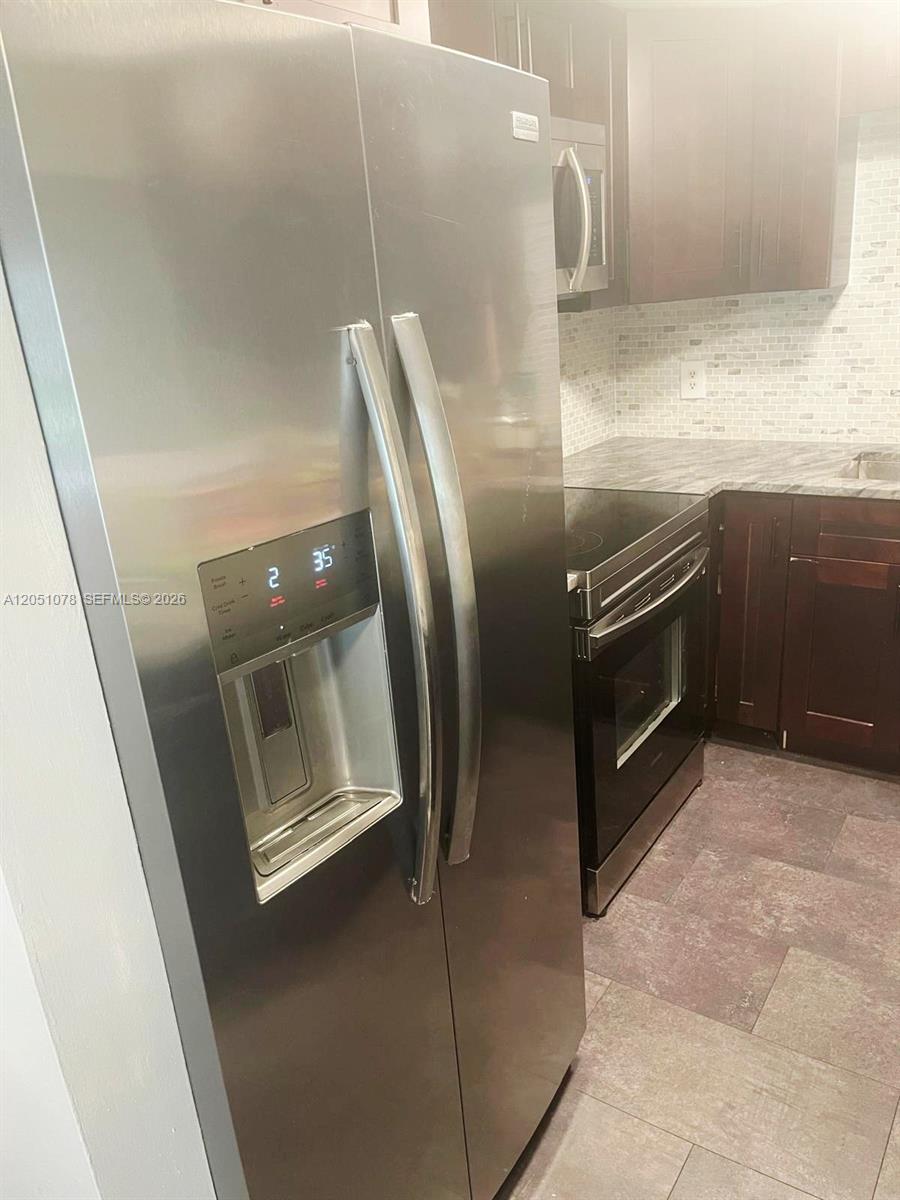 A stainless steel side-by-side refrigerator stands in a kitchen with dark wood cabinets — LAUDERHILL, FL