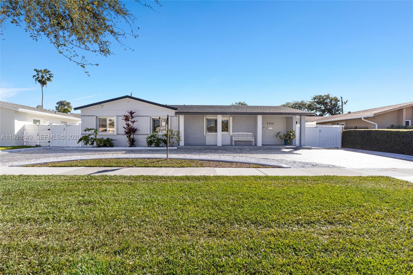 A single-story house with a paved driveway, white bench, and green lawn under blue sky — 9390 SW 190th St, Cutler Bay FL 33157, CUTLER BAY, FL